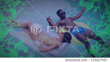 Reclining couple wearing swimwear holding hands on silver yellow floats in pool, neon-green overlay 135827487