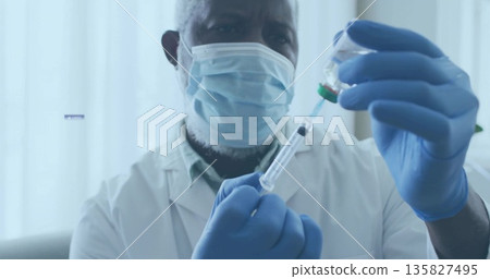 Drawing liquid from vial into syringe healthcare worker in lab coat, mask and gloves in clinic Drawing liquid from vial into syringe healthcare worker in lab coat, mask and gloves in clinic 135827495