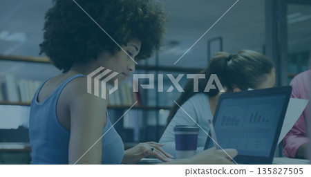 Leaning woman with curly hair typing on laptop in modern workspace, purple coffee cup, copy space 135827505