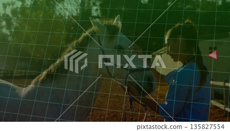 Asian woman holding halter and caressing white horse in riding arena with wooden fence, copy space 135827554