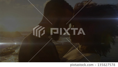 Couple touching foreheads on rocky shoreline at sunset, with glowing ocean waves and lens flares Couple touching foreheads on rocky shoreline at sunset, with glowing ocean waves and lens flares 135827578