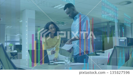 Pointing woman in yellow sweater reviewing documents with man in blue shirt in office, with pen 135827596