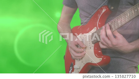 Playing guitarist pressing frets on red electric guitar in studio with green screen, copy space 135827710