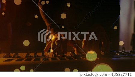 Pressing musician fingers in dark shirt playing keyboard under amber stage light, bokeh overlay 135827711