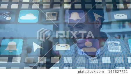 Smiling man wearing checkered shirt interacting with digital app icons in home office, with shelves Smiling man wearing checkered shirt interacting with digital app icons in home office, with shelves 135827751