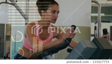 Cycling woman in pink top and leggings viewing data at gym, with stationary bike console charts Cycling woman in pink top and leggings viewing data at gym, with stationary bike console charts 135827755