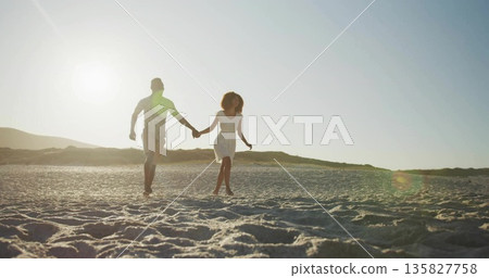 Holding hands couple running barefoot across rippled sandy beach at sunset, with distant dunes Holding hands couple running barefoot across rippled sandy beach at sunset, with distant dunes 135827758