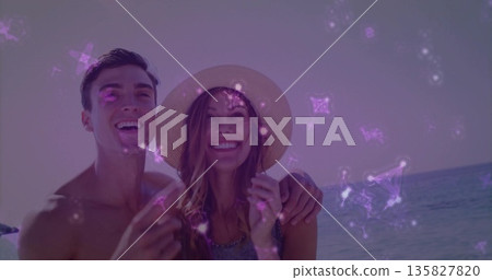 Smiling shirtless man hugging partner at beach edge, with straw sun hat under violet sparkle filter Smiling shirtless man hugging partner at beach edge, with straw sun hat under violet sparkle filter 135827820