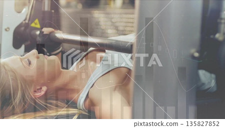 Female athlete in sports bra and gloves bench pressing on machine in gym, with digital overlay Female athlete in sports bra and gloves bench pressing on machine in gym, with digital overlay 135827852