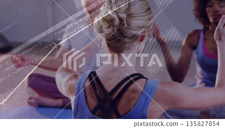 Stretching blonde woman wearing blue sports top raising arms overhead in studio, with yoga mats Stretching blonde woman wearing blue sports top raising arms overhead in studio, with yoga mats 135827854