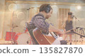 Male guitarist wearing plaid shirt, playing acoustic guitar in recording studio, with red drum kit 135827870