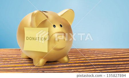 A golden piggy bank with a donation sticky note on a wooden table. Concept for charitable giving, fundraising, philanthropy, and financial aid for a good cause A golden piggy bank with a donation sticky note on a wooden table. Concept for charitable giving, fundraising, philanthropy, and financial aid for a good cause 135827894