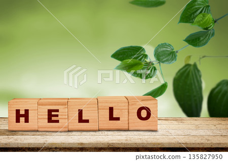 A friendly greeting spelled with wooden cubes on a rustic surface. The word HELLO is set against a beautiful blurred green garden background, perfect for a welcoming message 135827950