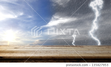 Empty rustic wooden table with a background of contrasting weather, showing a bright sunny sky on one side and a dark stormy sky with rain and lightning on the other 135827953