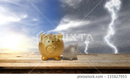 Two piggy banks on a wooden table against a split sky of sunshine and storm, symbolizing financial security, risk management, and saving for a rainy day 135827955