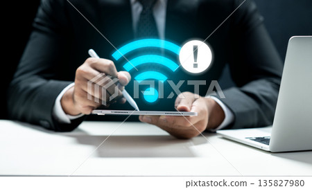 A businessman in a suit holding a tablet that displays a glowing blue Wi-Fi icon with an exclamation mark warning sign, indicating no internet connection or technical connectivity issues A businessman in a suit holding a tablet that displays a glowing blue Wi-Fi icon with an exclamation mark warning sign, indicating no internet connection or technical connectivity issues 135827980