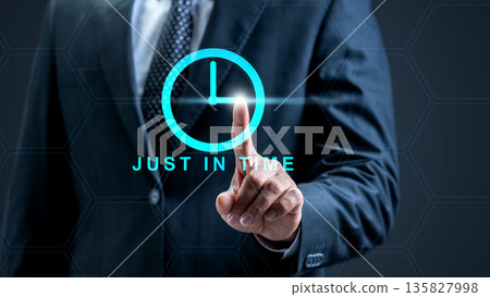 A businessman interacts with a glowing cyan clock interface featuring the words Just In Time, representing efficiency, lean management, and supply chain optimization in a modern corporate world 135827998