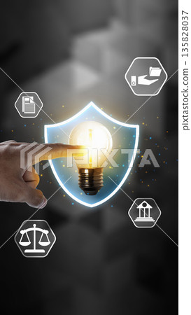 Hand touching a glowing lightbulb inside a shield, surrounded by legal icons. Represents intellectual property protection, patent law, innovation security, and copyright concept 135828037