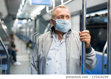 Mature passenger wearing protective mask rides in an underground metro car Mature passenger wearing protective mask rides in an underground metro car 135828294