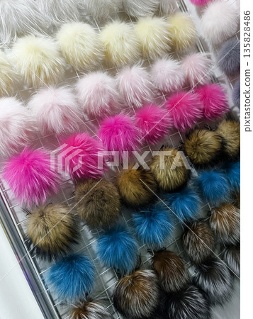 Display of colorful fur pom poms in a craft store showing various colors and sizes hanging in rows under bright lights Display of colorful fur pom poms in a craft store showing various colors and sizes hanging in rows under bright lights 135828486