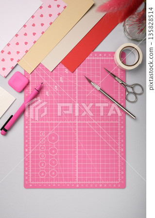 Pink cutting mat surrounded by colored paper and craft tools on desk. Creative workspace for art and handmade design preparation. Pink cutting mat surrounded by colored paper and craft tools on desk. Creative workspace for art and handmade design preparation. 135828514