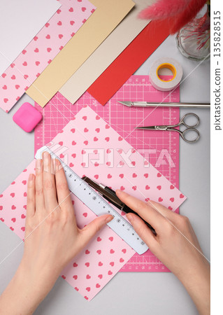 Hands working with colorful paper using a precision knife on pink cutting mat. Tools for paper crafts. Ruler, pencil, scissors, tape, eraser Hands working with colorful paper using a precision knife on pink cutting mat. Tools for paper crafts. Ruler, pencil, scissors, tape, eraser 135828515