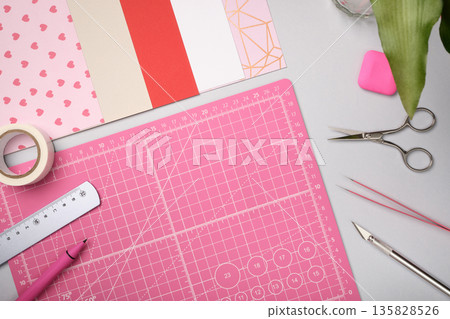 Pink workspace for paper crafts. Colored sheets, cutting mat, tape, pencil, knife, eraser. Space for text. Pink workspace for paper crafts. Colored sheets, cutting mat, tape, pencil, knife, eraser. Space for text. 135828526