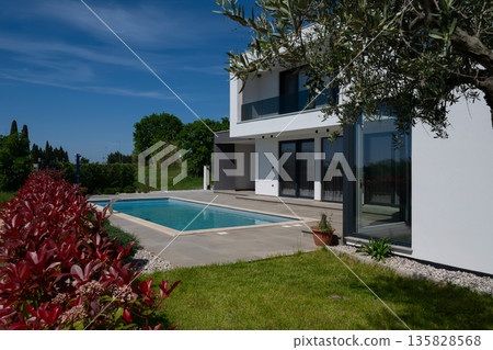 Modern luxury villa with swimming pool and clean minimalist architecture under a blue sky. Contemporary residential exterior featuring large windows, terrace, and elegant outdoor living space Modern luxury villa with swimming pool and clean minimalist architecture under a blue sky. Contemporary residential exterior featuring large windows, terrace, and elegant outdoor living space 135828568