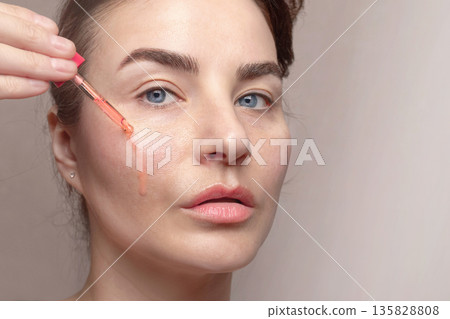 Caucasian woman applies serum from a pipette to her face. Caucasian woman applies serum from a pipette to her face. 135828808