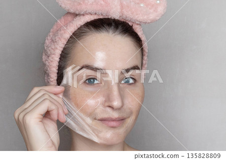 Caucasian woman makes a cosmetic Peel Off Mask. She removes the film mask with her hand Close up, copy space photo Caucasian woman makes a cosmetic Peel Off Mask. She removes the film mask with her hand Close up, copy space photo 135828809