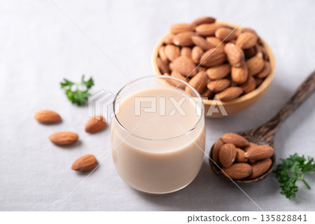 Glass of almond milk and almond nuts on white fabric background Glass of almond milk and almond nuts on white fabric background 135828841