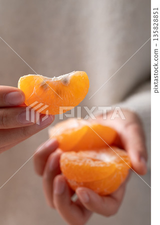Peeled Mandarin orange fruit holding by hand and eating 135828851