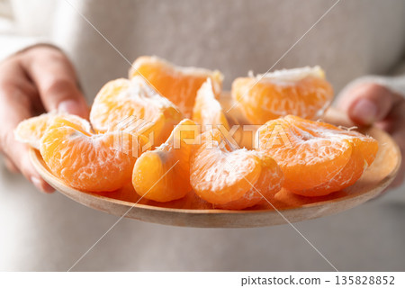 Peeled Mandarin orange fruit holding by hand and eating 135828852
