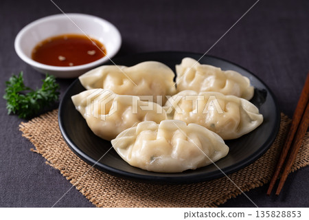 Close up of delicious steamed dumplings on a black plate served with sesame oil dipping sauce Close up of delicious steamed dumplings on a black plate served with sesame oil dipping sauce 135828853