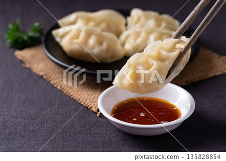 Close up of delicious steamed dumplings being dipped into sesame oil sauce with chopsticks Close up of delicious steamed dumplings being dipped into sesame oil sauce with chopsticks 135828854