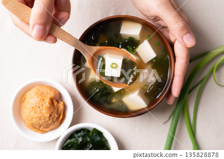 Top view of hand holding spoon and eating healthy Japanese miso soup with soft tofu and seaweed 135828878