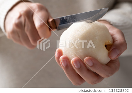 Close-up of a hand using a paring knife for cutting a fresh Asian pear Close-up of a hand using a paring knife for cutting a fresh Asian pear 135828892