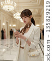 一位女商人正在華麗的大廳裡查看她的智慧型手機[職業女性] 135829219