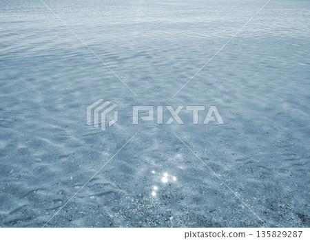 Clean transparent water on shallow sandy seashore with shells with shells on sunny summer day. Sun glare on surface of water. Small waves on sea coast. Nature backdrop. Natural background Clean transparent water on shallow sandy seashore with shells with shells on sunny summer day. Sun glare on surface of water. Small waves on sea coast. Nature backdrop. Natural background 135829287