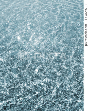 Clean transparent water on shallow sandy seashore with shells with shells on sunny summer day. Sun glare on surface of water. Small waves on sea coast. Nature backdrop. Natural background Clean transparent water on shallow sandy seashore with shells with shells on sunny summer day. Sun glare on surface of water. Small waves on sea coast. Nature backdrop. Natural background 135829292