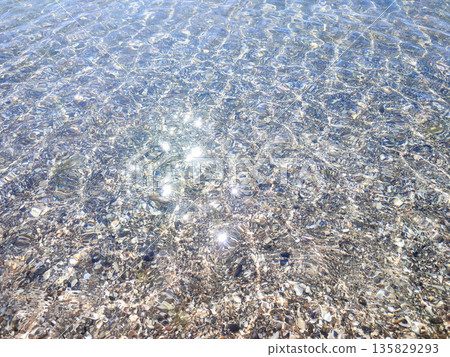 Clean transparent water on shallow sandy seashore with shells with shells on sunny summer day. Sun glare on surface of water. Small waves on sea coast. Nature backdrop. Natural background Clean transparent water on shallow sandy seashore with shells with shells on sunny summer day. Sun glare on surface of water. Small waves on sea coast. Nature backdrop. Natural background 135829293