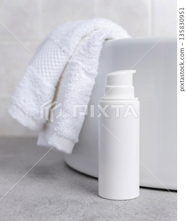 White cosmetic pump bottle on grey stone near white bath towel and basin close up, mockup 135830951