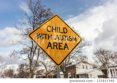Yellow road warning sign reading child with autism area in residential neighborhood under blue sky in United States 135831348