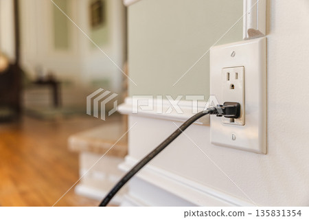 Power cable plugged into American electrical outlet in modern home interior, close view of wall socket and cord with soft blurred background 135831354