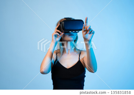 Female gamer interacting with virtual objects using VR headset, hand tracking and immersive gaming technology concept Female gamer interacting with virtual objects using VR headset, hand tracking and immersive gaming technology concept 135831858
