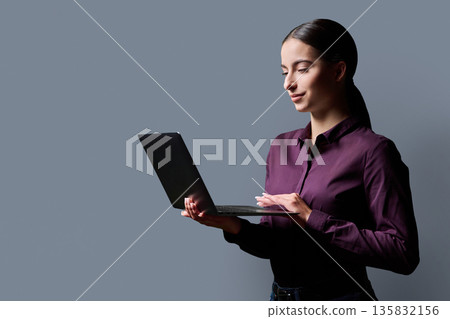 Portrait of smiling teenage girl using laptop on gray studio background Portrait of smiling teenage girl using laptop on gray studio background 135832156