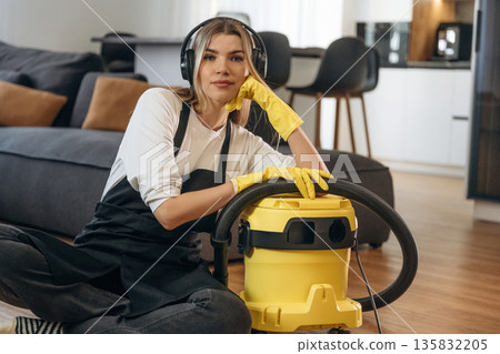 Sitting with vacuum cleaner. Female professional cleaning service worker is domestic room Sitting with vacuum cleaner. Female professional cleaning service worker is domestic room 135832205
