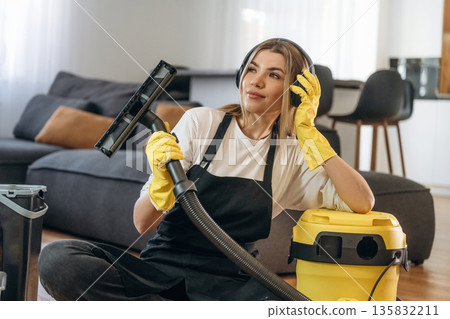 Yellow vacuum cleaner, sitting with it. Female professional cleaning service worker is domestic room Yellow vacuum cleaner, sitting with it. Female professional cleaning service worker is domestic room 135832211