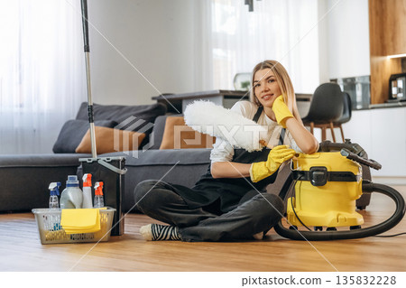 Resting, sitting on the floor. Female professional cleaning service worker is domestic room Resting, sitting on the floor. Female professional cleaning service worker is domestic room 135832228