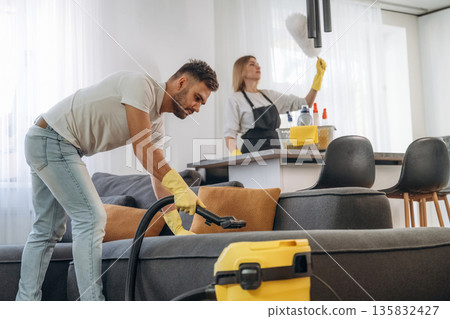 Modern yellow vacuum cleaner, busy. Two cleaning service workers are in domestic room Modern yellow vacuum cleaner, busy. Two cleaning service workers are in domestic room 135832427